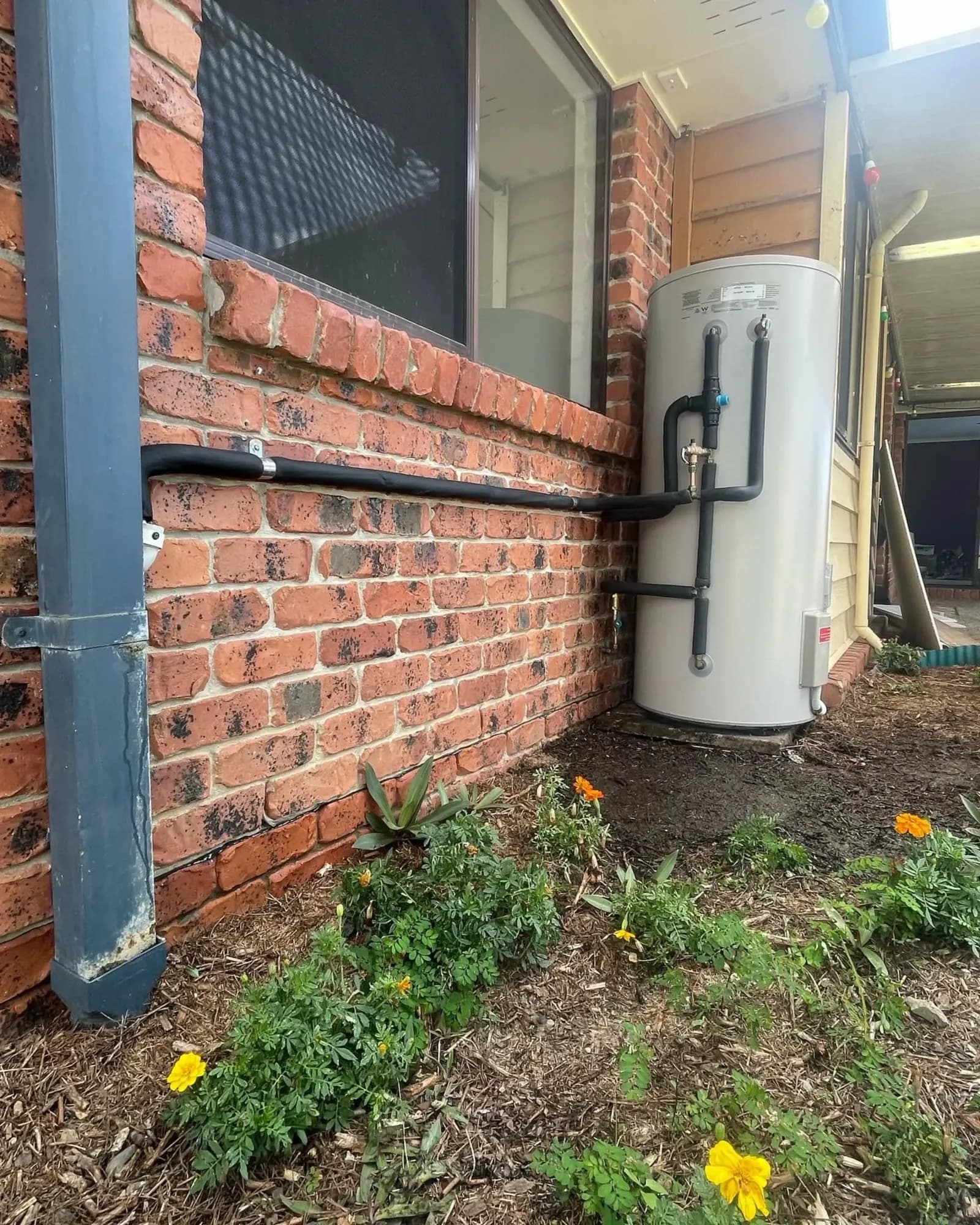 Hot water system installed in a garden bed beside a brick house