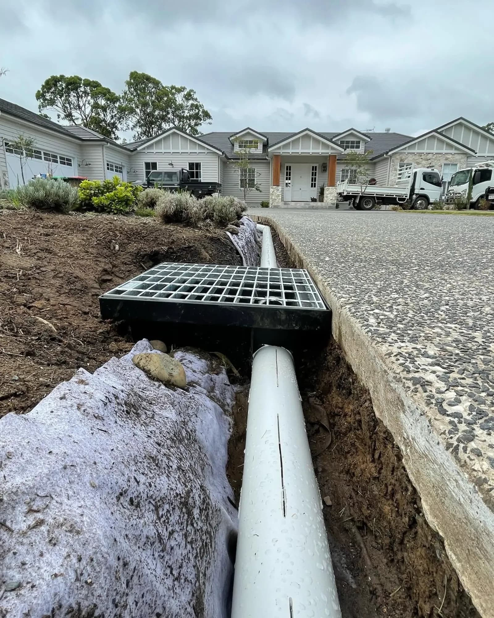 Grated stormwater pit and pipe being installed beside a driveway