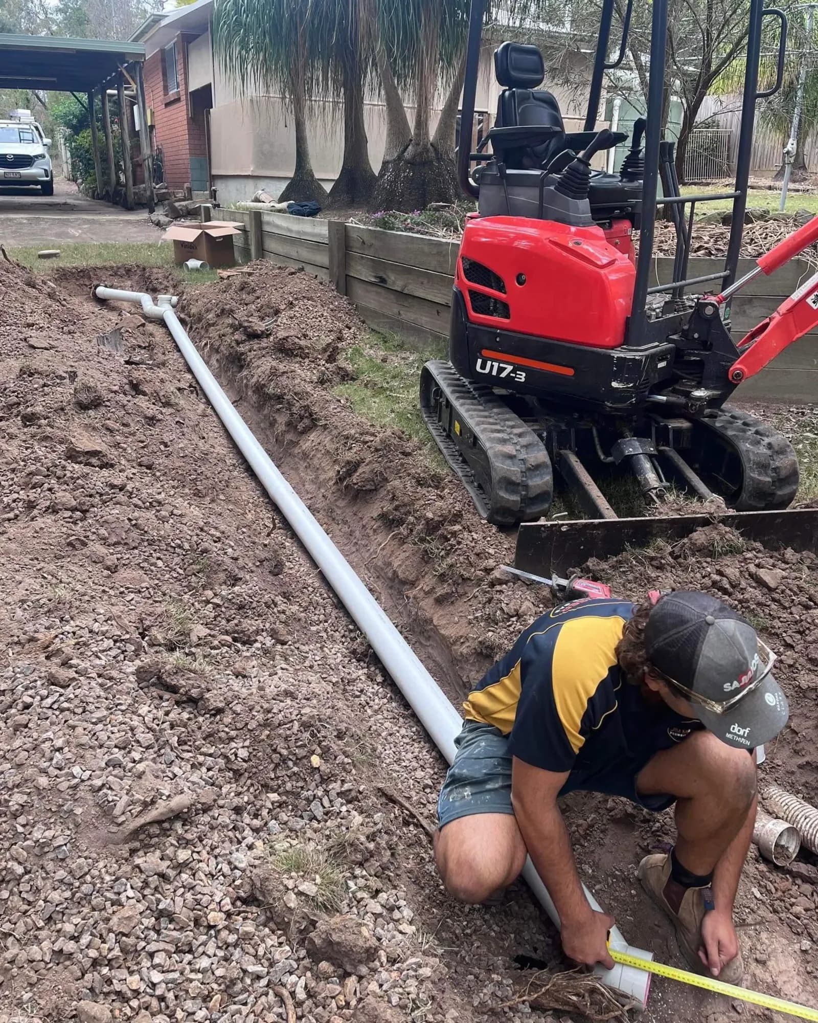 Plumber laying a new drain line with an excavator behind