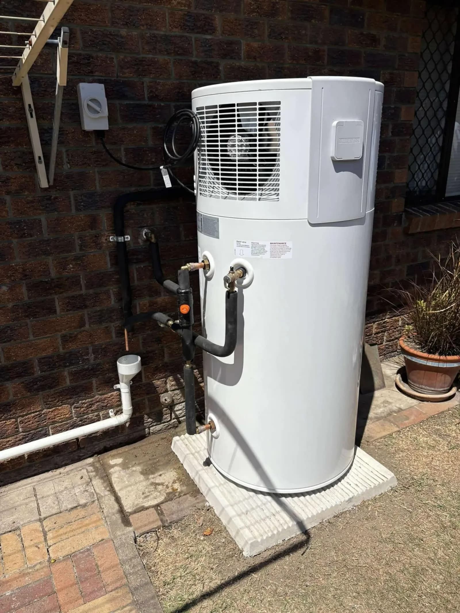 Heat pump hot water unit installed beside a brick house