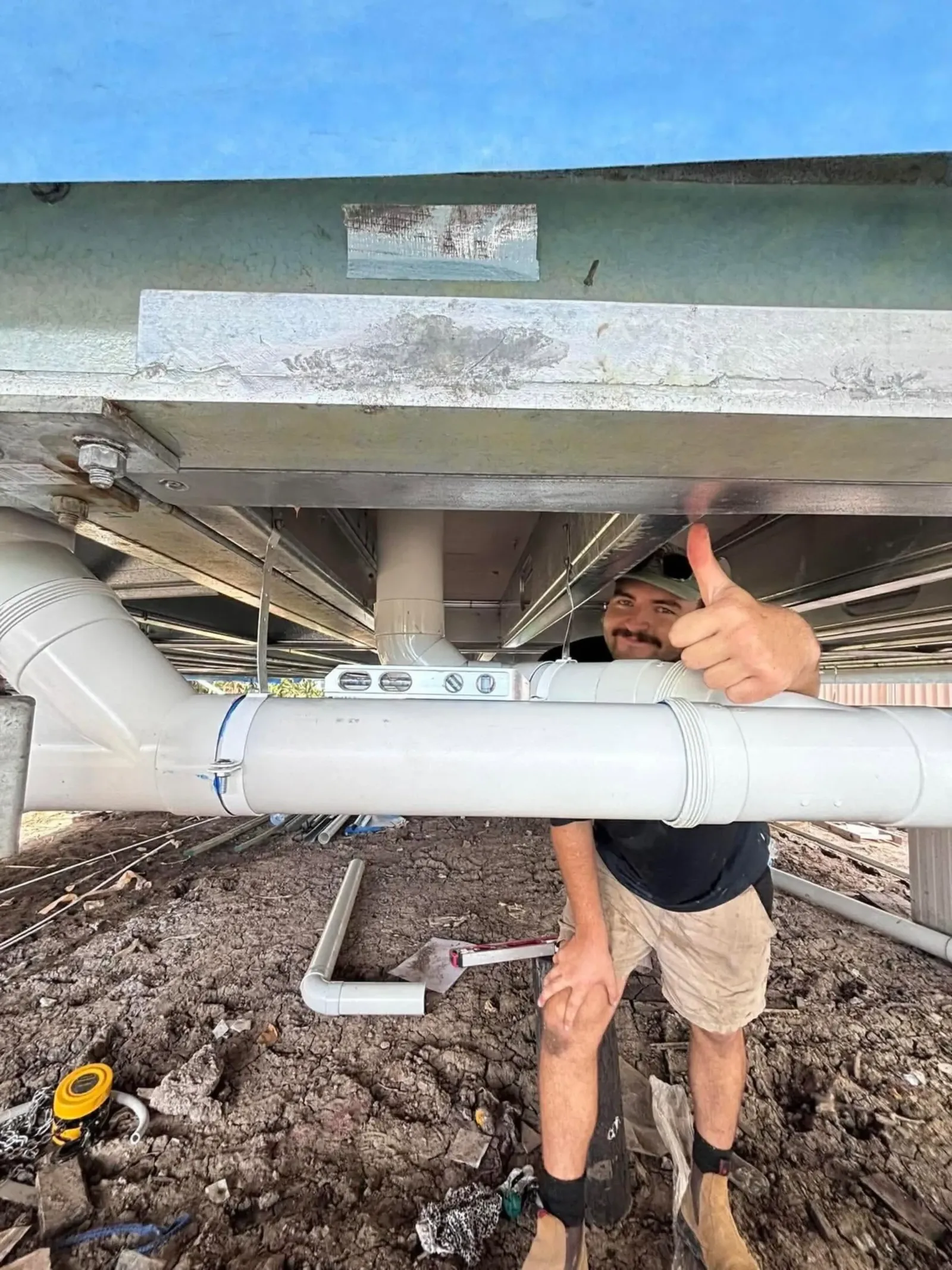 Plumber fitting new PVC drain pipe under a house