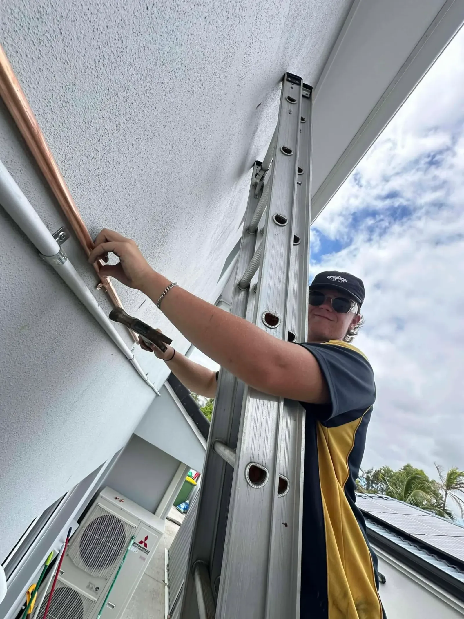 Plumber on a ladder fixing pipework to an outside wall