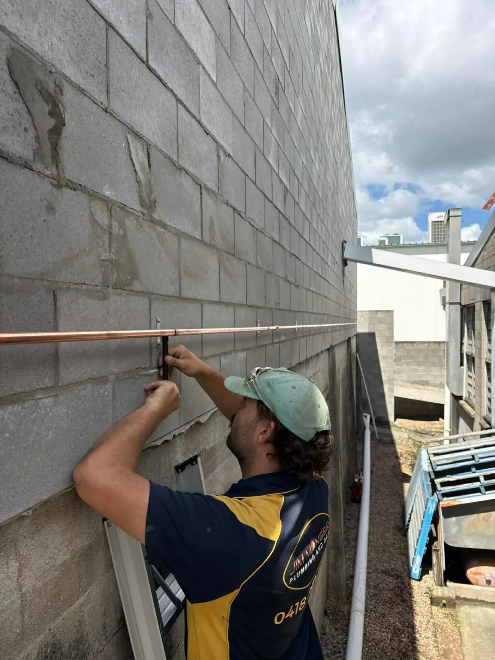 Plumber fixing copper pipe to a block wall