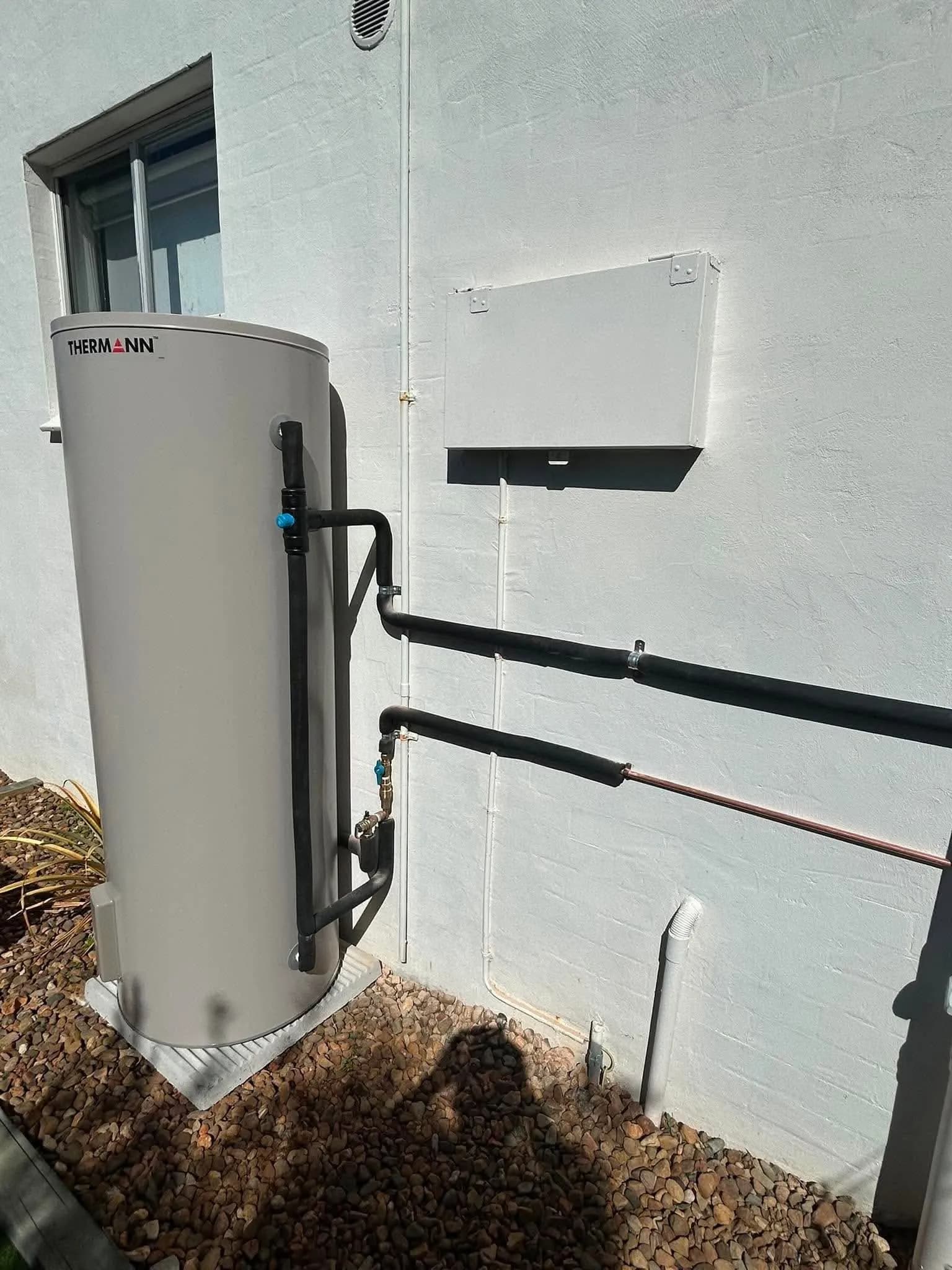 Electric hot water tank installed against a rendered wall