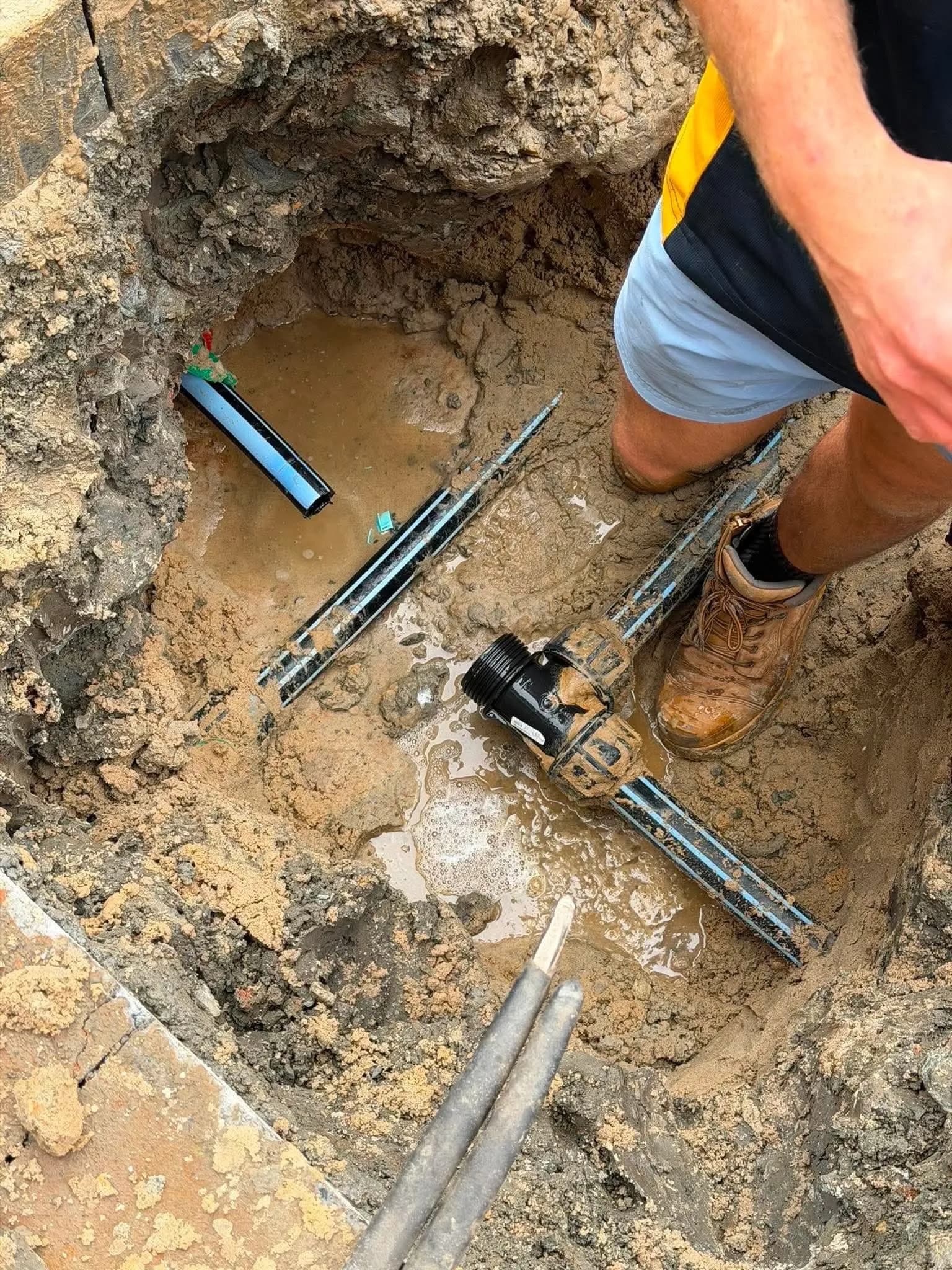 Underground water pipe being repaired in a muddy hole