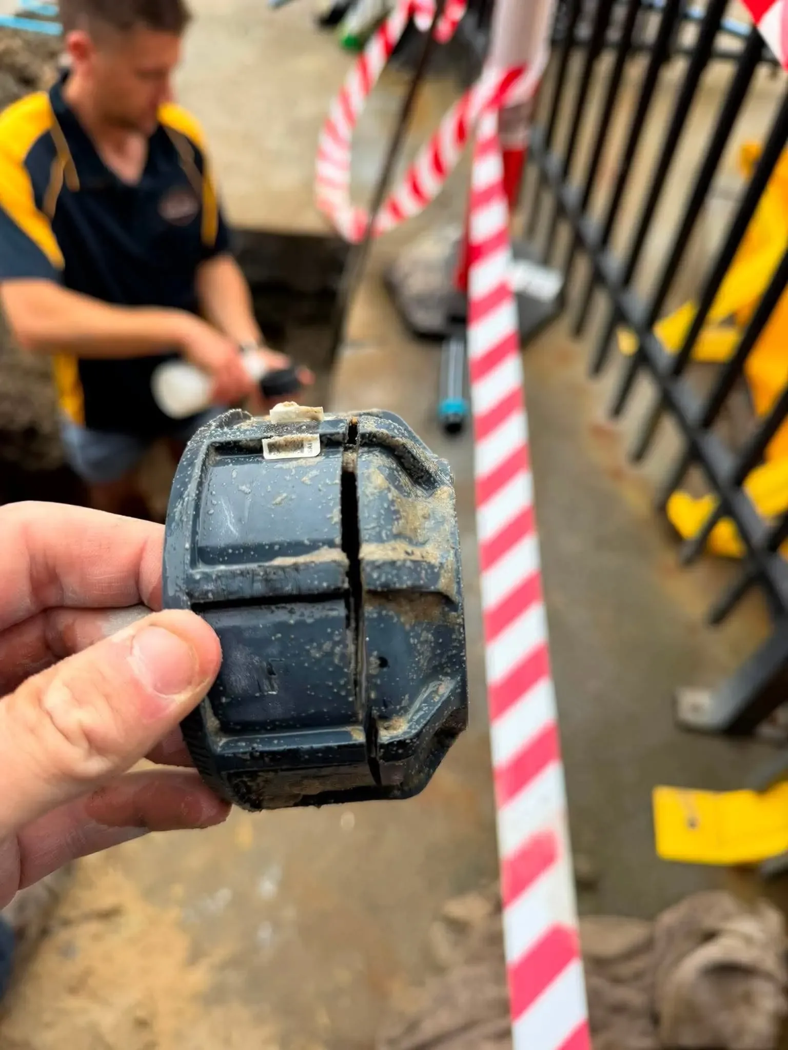 Plumber holding a damaged water fitting at a taped-off site